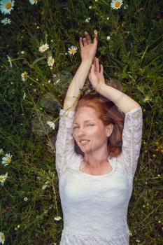 Beautiful young girl with curly red hair in camomile field