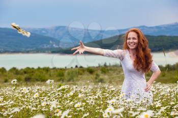 Beautiful young girl with curly red hair in camomile field