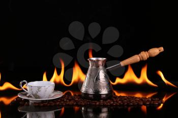 Turk and cup on coffee beans on a background of fire, black background. CONCEPT vivacity and energy
