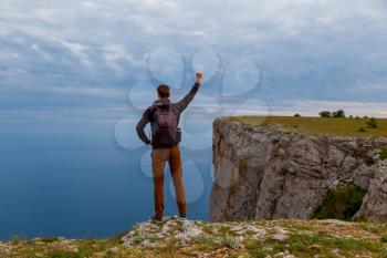 Man on top of mountain. Conceptual design.Young man with backpack standing with raised hands on top of a mountain and enjoying valley view. The idea of victory and the championship