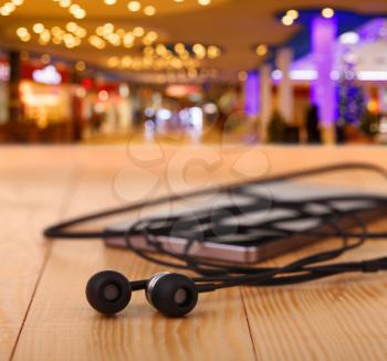 mobile phone with pair of earphone on wooden table on night city background