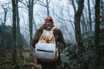 man walking on a dark path through a spooky forest. Hipster with a backpack behind his back goes on a trip