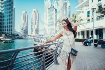 Happy beautiful unrecognizable tourist woman in fashionable summer white dress enjoying in Dubai marina in United Arab Emirates. Luxury and comfortable tourism season in UAE.