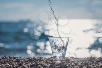 splashing water in a glass by the sea. Beautiful glass with ice and pure mineral water