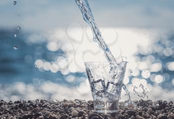 splashing water in a glass by the sea. Beautiful glass with ice and pure mineral water