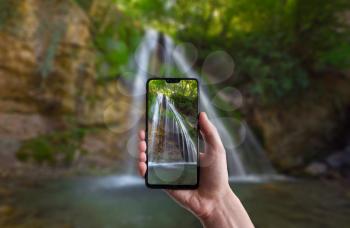 A man makes a photo on a smartphone, beautiful landscape of waterfall scenery in the middle of green forest. Beautiful Crimean waterfall Dzhur-dzhur