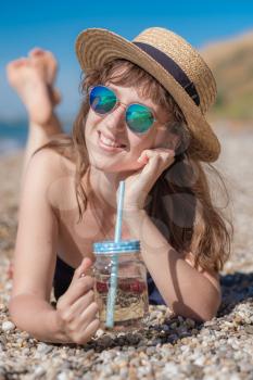 Pretty young woman drinking cocktail on the beach. Attractive girl offering a drink. Beautiful woman drinking lemonade