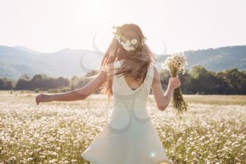 Beautiful young girl smiling over chamomile field. Carefree happy brunette woman with healthy long hair having fun outdoor in nature.