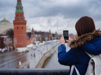 Young asian beautiful woman tourist taking pictures on mobile phone on the background of Moscow Kremlin, Russia