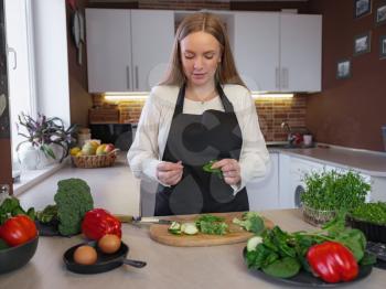 A young blonde happy lady standing in the kitchen while cooking healthy food. Healthy Lifestyle Concept. Cooking at home. cutting vegetables for cooking