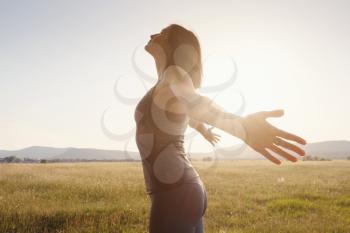 Young woman spreading hands with joy and inspiration facing the sun. She is enjoying serene nature workout vacation outdoors.