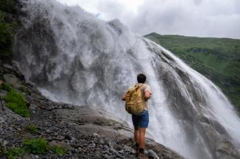 Waterfall Landscape and male Traveler enjoying waterfall view. active vacations into the wild harmony with nature. Image for hiking or climbing. Alibek Waterfall, North Caucasus, Dombai, Russia.