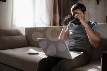 Funny man looking searching binoculars a laptop on the table working at home office. Job search online. searching idea and concept