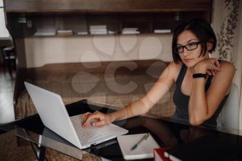 Young asian female student in glasses using laptop, communicates on internet. Cozy office workplace, remote work, E learning concept.