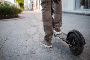Close up of man riding black electric kick scooter at cityscape at sunset. Electric urban transportation concept image