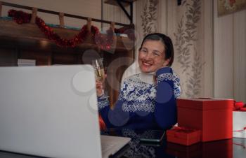 Christmas online congratulations. Smiling asian woman in blue sweater using computer for video call friends and parents. Emotional face.