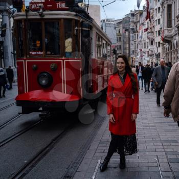 Fashion style portrait of young beautiful young woman posing at city street in Taksim, steet with red train. A girl walks through winter Istanbul.