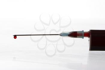Macro view of drop of blood from syringe over white background. Blood chemistry. Blood test for viruses.