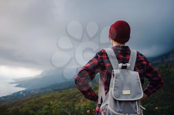Stylish hipster asian woman with hat walking on top of mountains. Happy young woman with a backpack exploring the misty mountains. The concept of travel and wanderlust. Amazing atmospheric moment