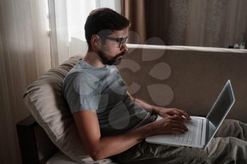 Remote Job. Man Working On Laptop Sitting On Sofa At Home. Copy Space For Text. freelancer hipster works from home, studying or communicating with partners