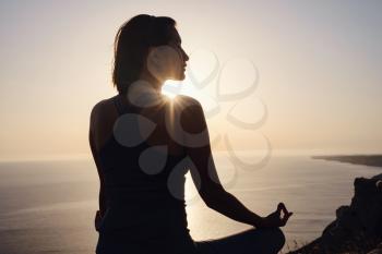Young woman practicing yoga over sunset sea. meditation in the lotus position. Yoga silhouette. Harmony and meditation concept. Healthy lifestyle
