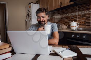 Portrait of happy man having a cup of coffee in kitchen. The guy works from home.