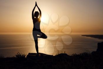 The woman with yoga posture on the mountain at sunset Silhouette of gorgeous young woman practicing yoga outdoor. wellness, healthcare, sport and lifestyle concept