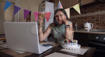 Lady celebrating birthday online in quarantine time. Woman celebrating her birthday through video call virtual party with friends. Authentic decorated home workplace. Coronavirus outbreak 2020.