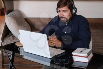 Happy male student online teacher wear headphone talk video calling, looking at laptop computer screen, do conference chat communicate with skype tutor, distance education e learning course at home