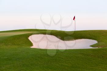 Red flag of golf hole above sand trap or bunker on beautiful course at sunset