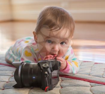 Young caucasian baby girl lying on carpet or rug and playing with an expensive camera as a budding photographer