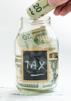 Caucasian hand putting money into glass jar on white background with black chalk label or panel and used for saving US dollar bills for a tax bill