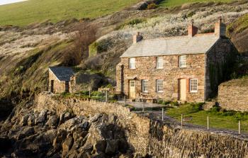 View of stone cottage and hillside in late evening sunlight in Port Quin, Cornwall, England, UK