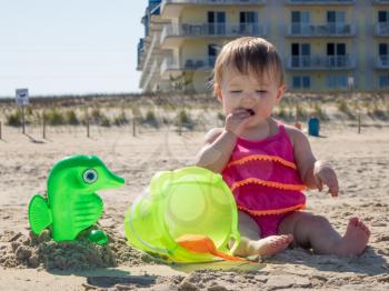 Cute caucasian baby girl on sandy beach tasting sand for the first time in Ocean CIty, Maryland, USA