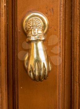 Front view of brass door knocker shaped like a hand on old wooden door
