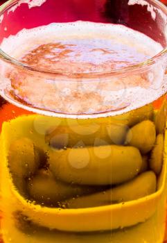 Green olives show through the sides of glass of beer in a traditional tankard or mug against red tablecloth background