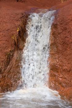 Small waterfall in stream causing erosion into red rocks near the Grand Canyon of the Pacific or Waimea Canyon on island of Kauai in the Hawaiian islands