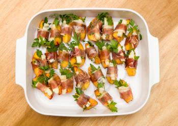 White plate full of home made appetizers with peach slice and gorgonzola cheese wrapped by strip of prosciutto ham