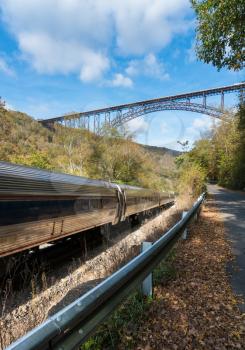 Railway and train alongside river underneath the high arched New River Gorge bridge in West Virginia