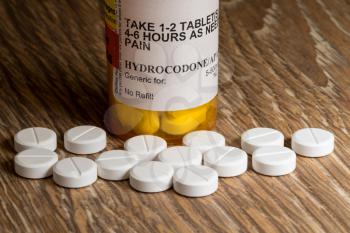 Close photo of prescription bottle for Hydrocodone tablets and pills on wooden table for opioid epidemic illustration
