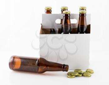 Five beer bottles in cardboard carrier with side of container facing camera and single bottle lying on table with caps