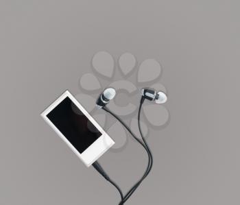 Small white portable MP3 digital music player with earbuds against a grey background