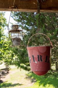 Old worn fire bucket and oil lamp hanging from rafters of log cabin