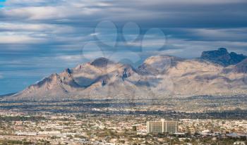 Downtown area of Tucson in Arizona with the sun lighting the buildings while storm clouds gather over distant Santa Catalina mountain range