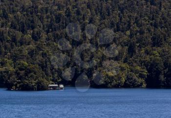 Small cabin and power boat in very remote setting below steep forest in Doubtful Sound on South Island of New Zealand