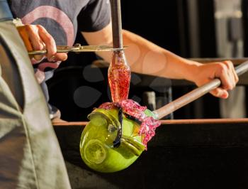 Glass blower artists work on adding decoration to ornate green glass bottle or bowl