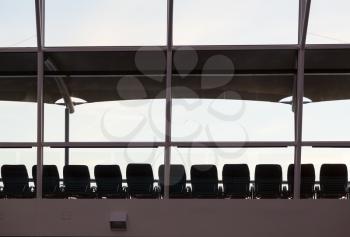 Silhouettes of deck or beach recliner chairs in a line under a sun shade on deck of cruise ship on a grey cloudy day