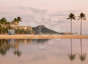 Panorama of the skyline of Waikiki at dawn taken with a long exposure to blur out movement in the water and provide a reflection of Diamond Head in Hawaii