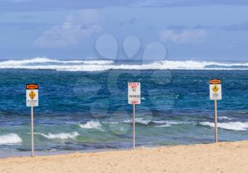 Three warning sign no swimming and strong currents in treacherous winter waters on Tunnels Beach in Kauai Hawaii