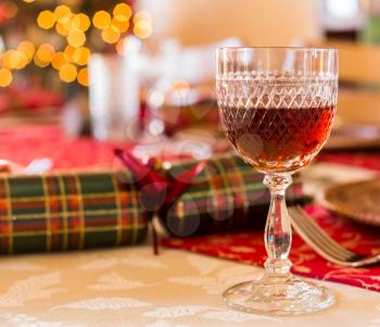 Christmas sherry in cut glass goblet on table set for Christmas lunch with crackers and decorated tree in background